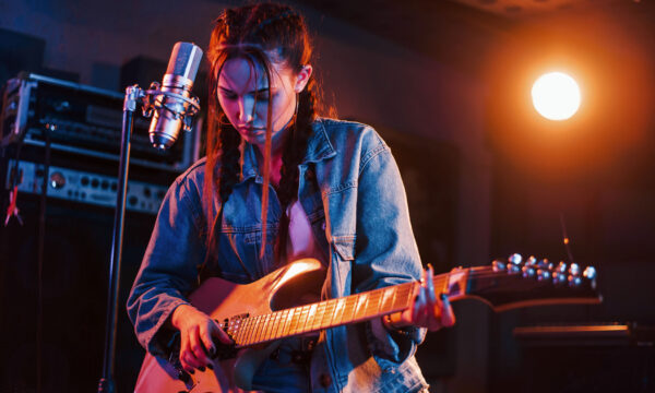 Young beautiful female performer with guitar singing and rehearsing in a recording studio.